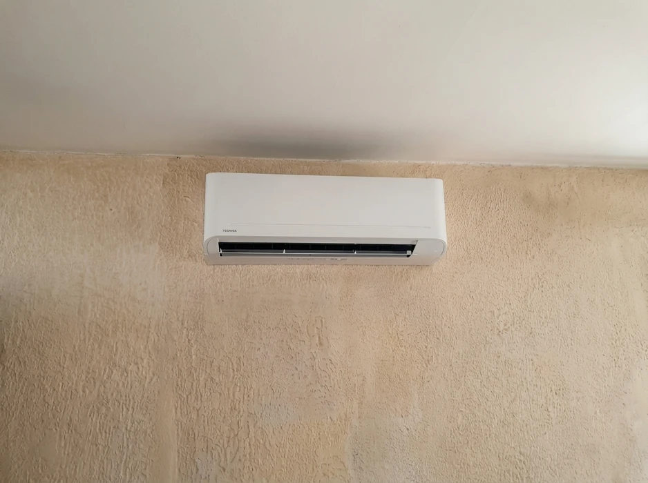 Unité intérieure de climatisation murale réversible de marque Toshiba, montée en hauteur sur un mur en crépi beige texturé