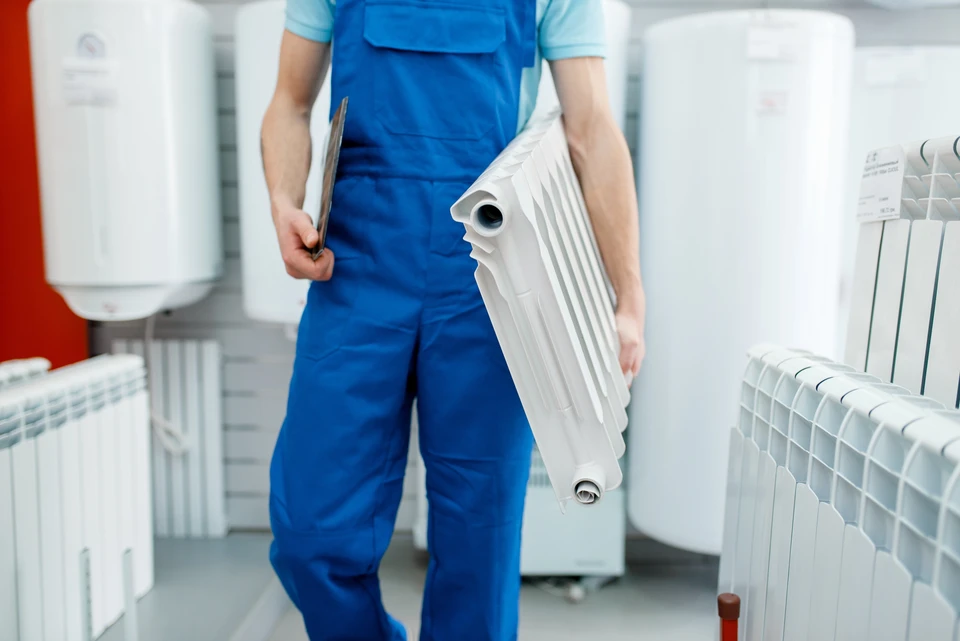 Technicien en plomberie chauffage installant un radiateur à ailettes blanches dans un intérieur résidentiel
